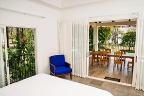 Una habitación con una cama, una silla azul, una mesa de comedor con sillas y vistas a un jardín a través de una puerta corredera.