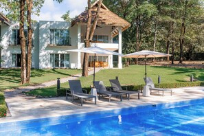A modern two-story house with a swimming pool, outdoor seating, and a thatched-roof structure.