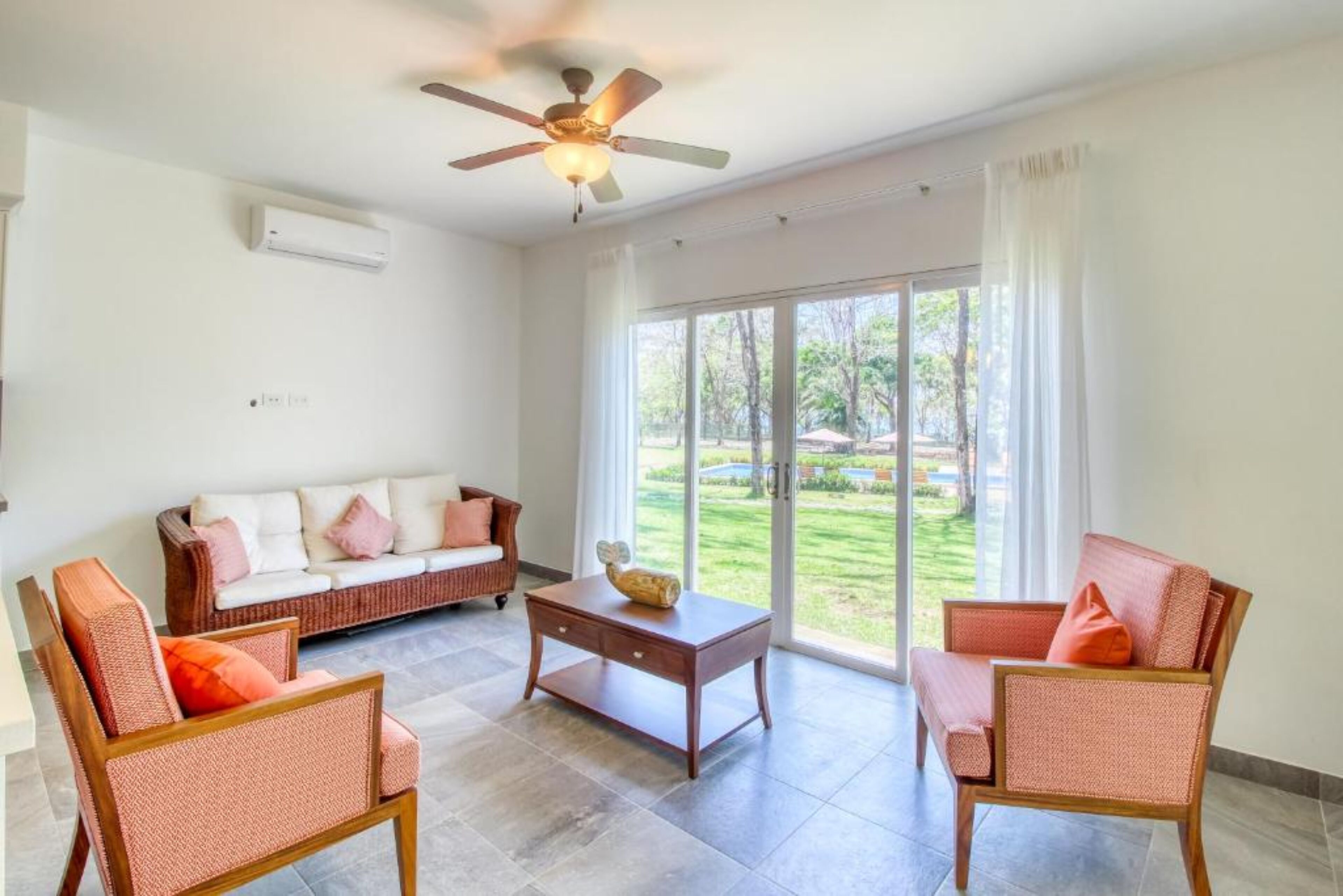 A spacious living area with a ceiling fan, a sofa, two armchairs, and a coffee table.