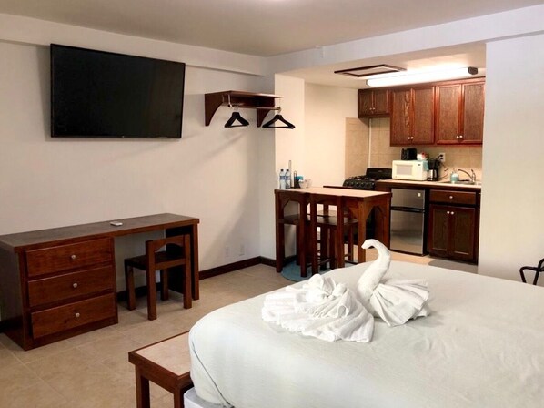 Una habitación de hotel con cama, escritorio, silla, televisor y kitchenette.