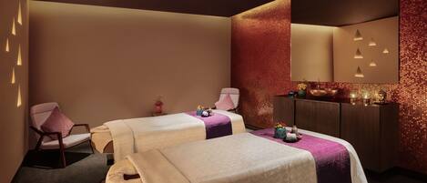 Un cuarto de spa con dos camas, una silla, un espejo y un detalle decorativo en la pared.