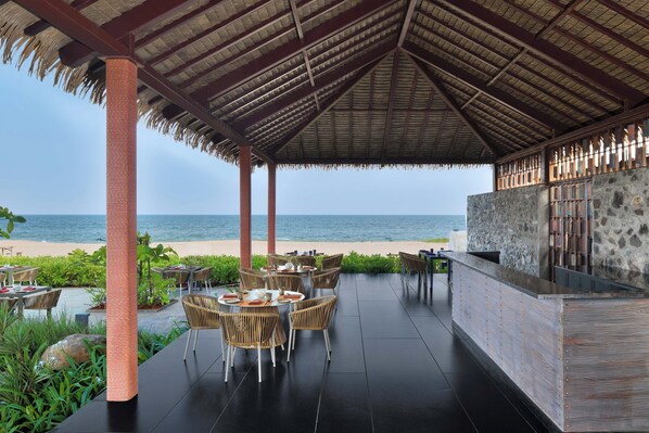 Un espace extérieur aménagé avec des tables et des chaises, un mur en pierre et une vue sur la plage.