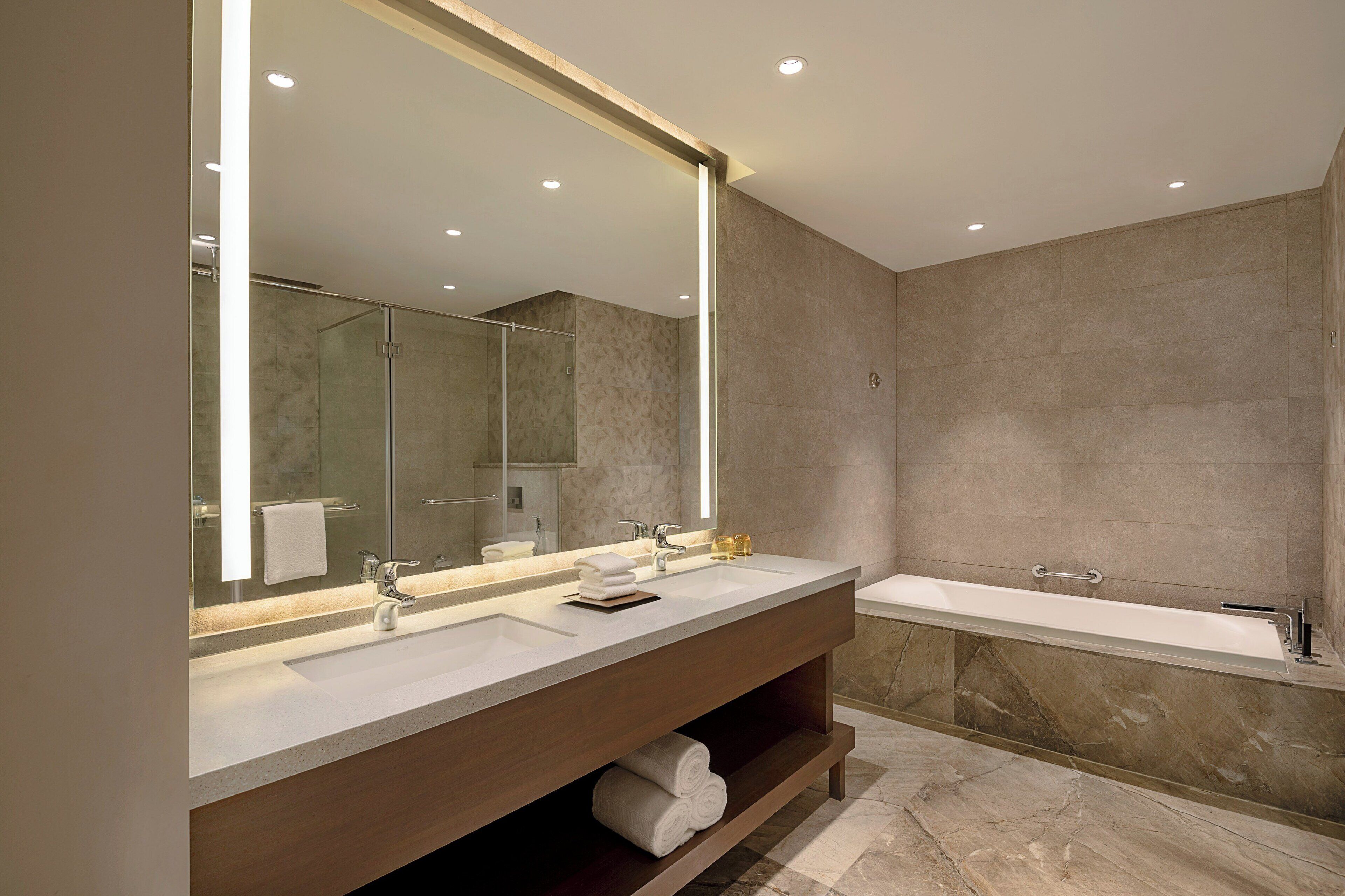A modern bathroom with a large mirror, two sinks, a bathtub, and a vanity with shelves.