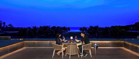 A couple dining at an outdoor table with a view of the ocean and palm trees.