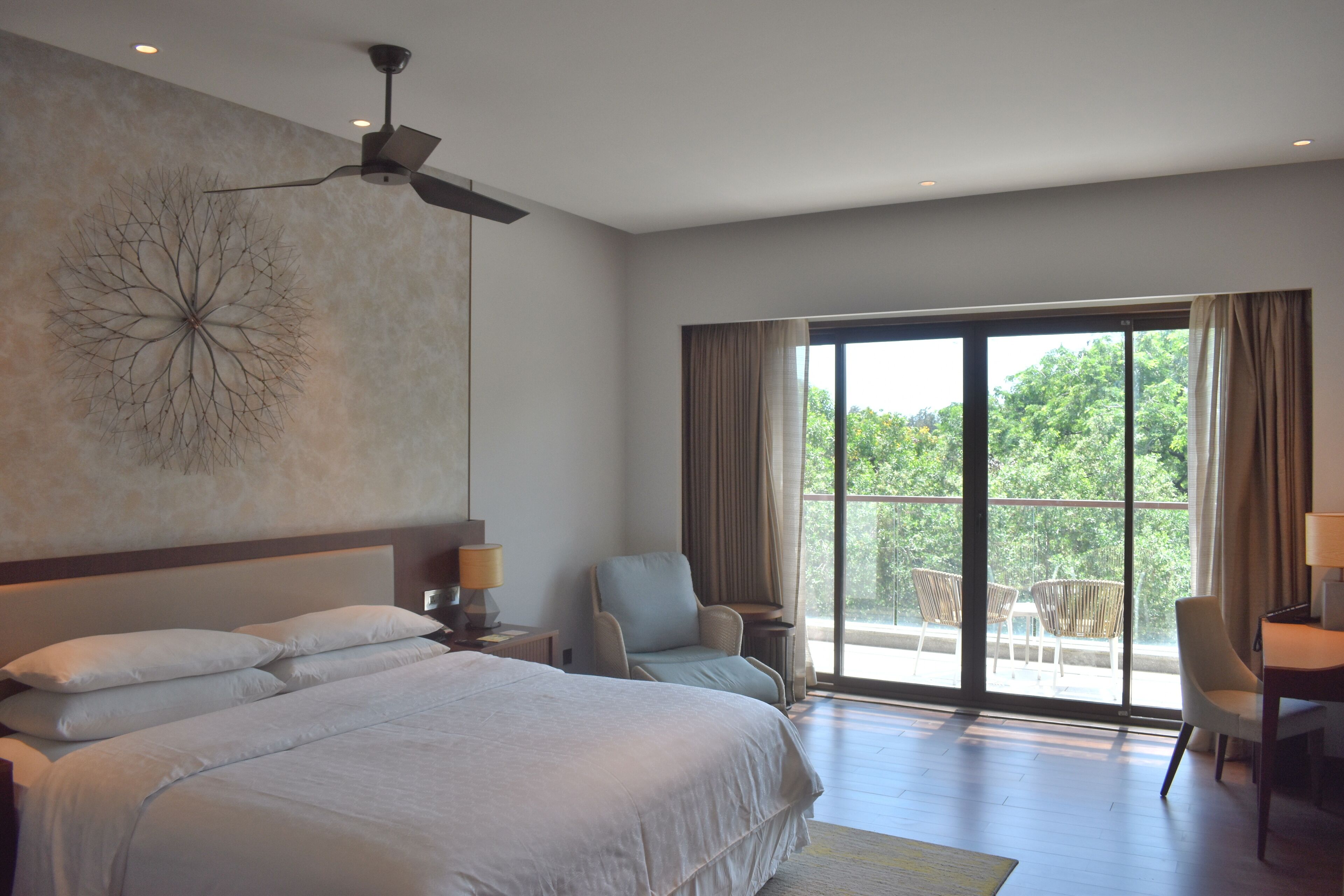 A spacious bedroom with a large bed, a ceiling fan, and a view of the outdoors through a large window.