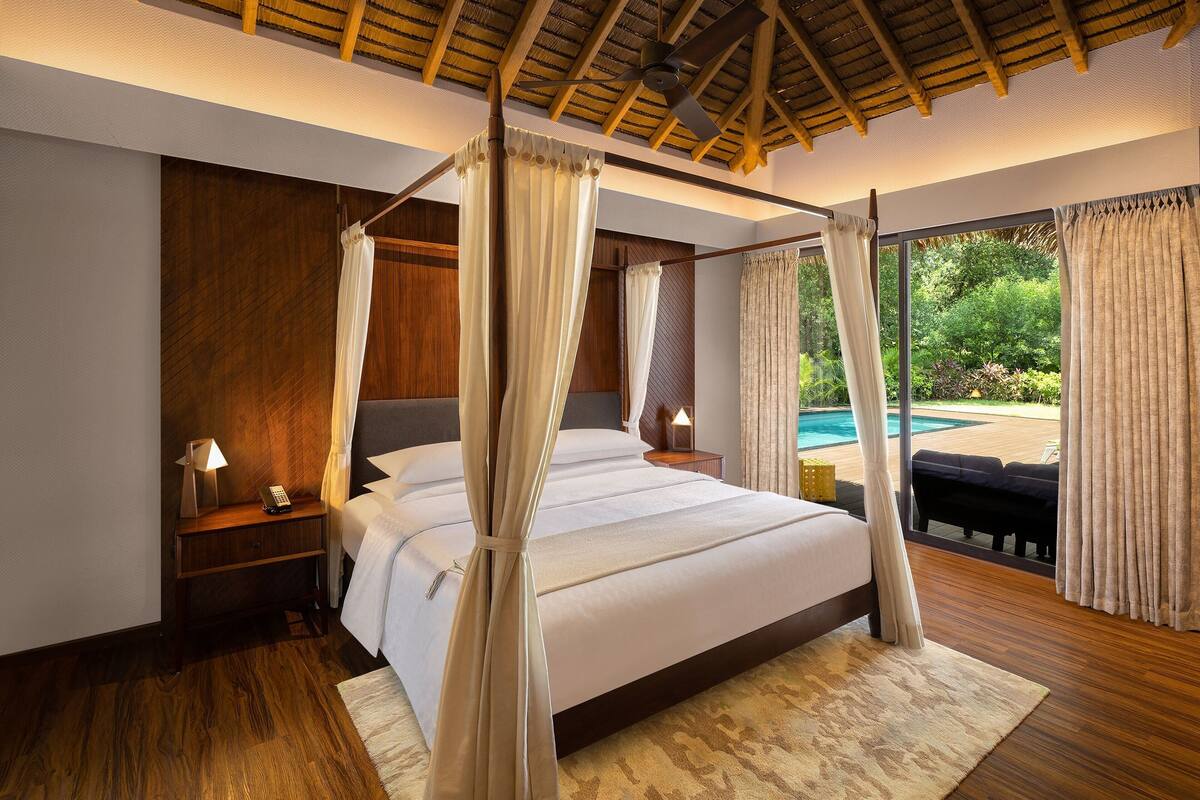 A bedroom with a four-poster bed, wooden flooring, and a view of a swimming pool.