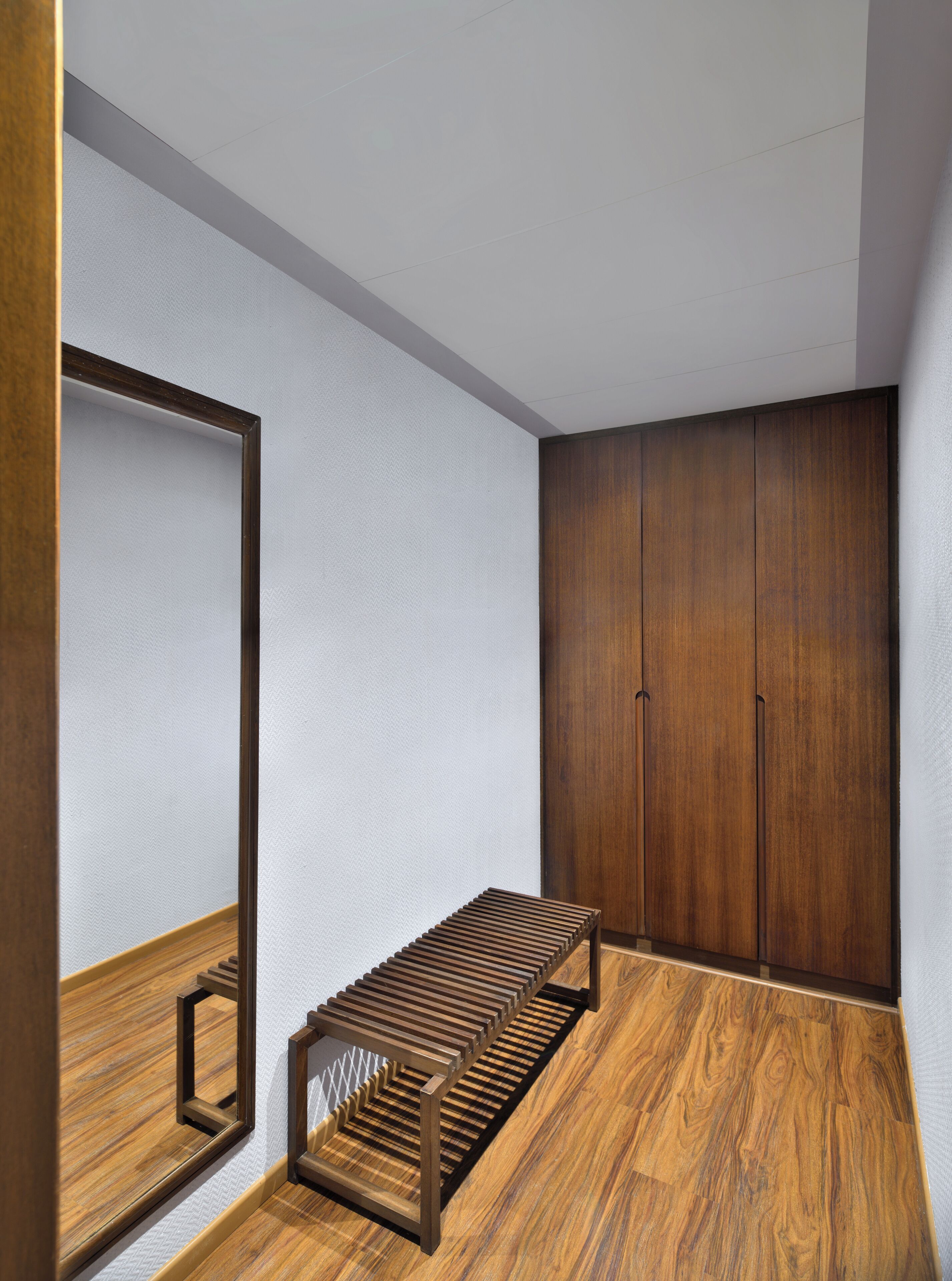 A room with a wooden bench, a large mirror, and wooden wardrobes.