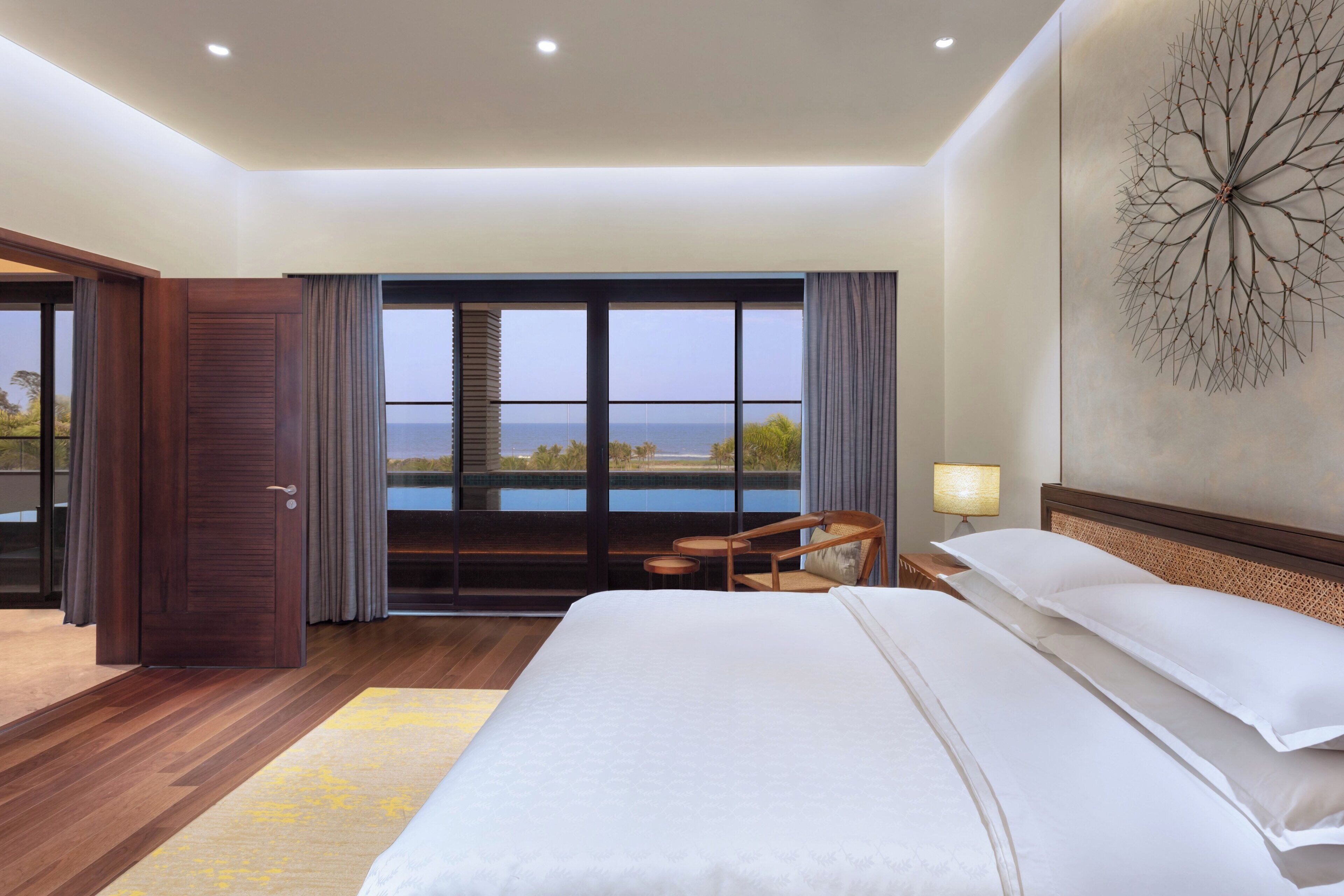 Une chambre d’hôtel avec un grand lit, une vue sur la mer, une porte en bois et une œuvre d’art accrochée au mur.