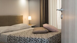 A neatly made bed with patterned bedding, a bedside lamp, and a window with curtains. - San Peter Angels Two (Rome)