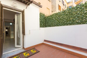 Una entrada residencial con puerta, un pequeño patio con azulejos y un seto verde.