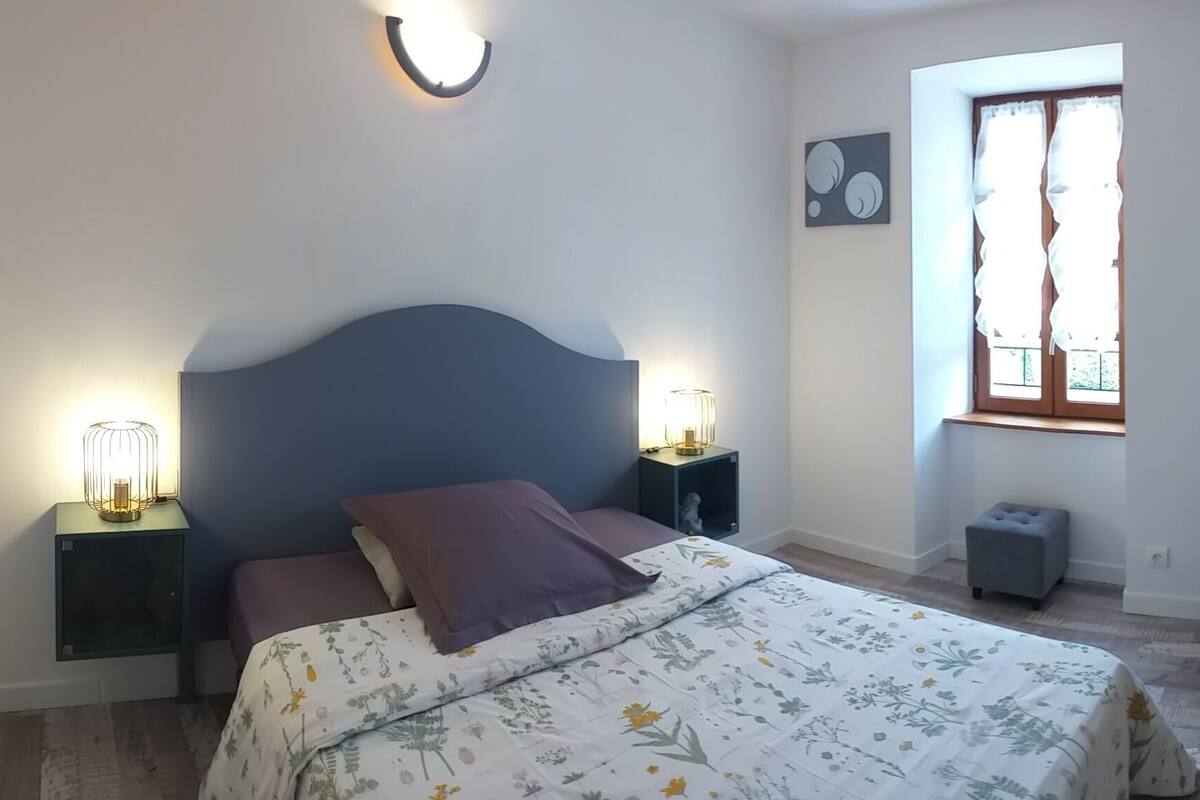 A bedroom with a bed, bedside lamps, a window, a chair, and a small table.