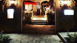 Entrada a un edificio de piedra con un arco de entrada, escalones que conducen a una puerta y dos letreros iluminados a ambos lados.