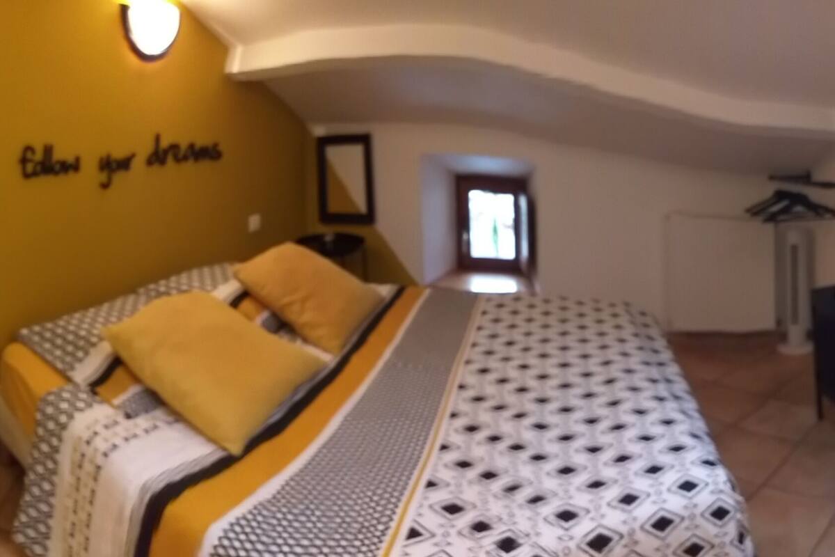 A room with a yellow sofa, a yellow armchair, a patterned bedspread, and a wall with the phrase "follow your dreams".