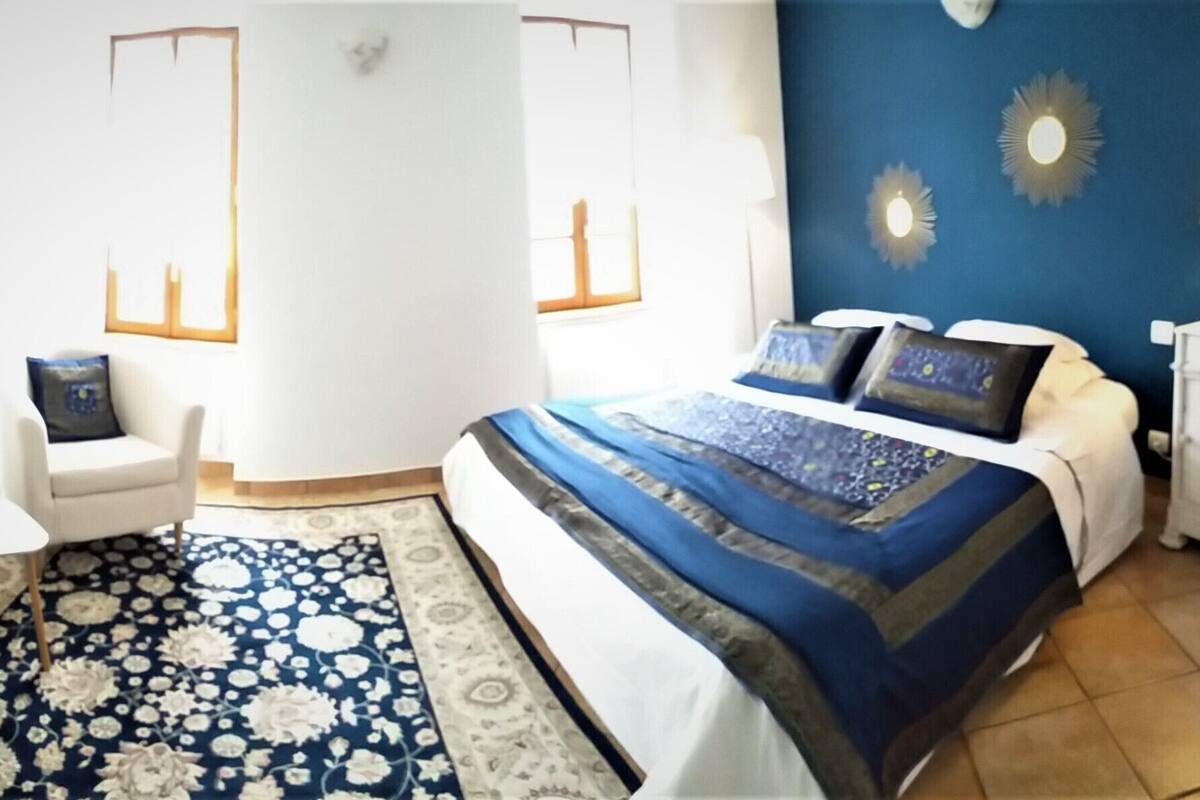 A bedroom with a large bed, a chair, a small table, and a nightstand.