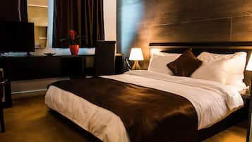 A hotel room with a large bed, a desk with a computer, a chair, a lamp, and a potted plant.