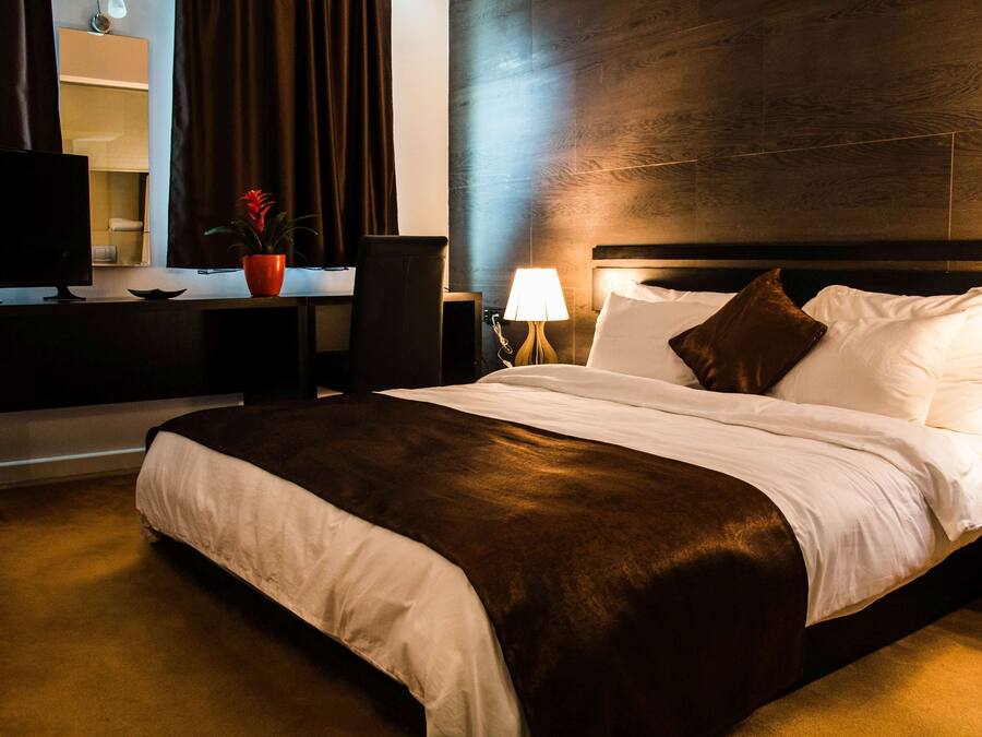 A hotel room with a large bed, a desk with a computer, a chair, a lamp, and a potted plant.