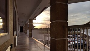 A covered corridor with tiled flooring, a railing, and a view of parked cars and a sunset. - Motel 6 Houston, TX - North (Houston)