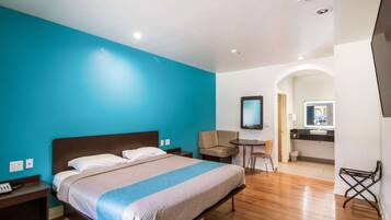Habitación de hotel con cama, escritorio, silla, espejo y baño visible a través de un arco.