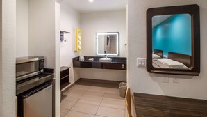 A compact hotel room with a kitchenette, a large mirror, and a view of the bed. - Motel 6 Houston, TX - North (Houston)