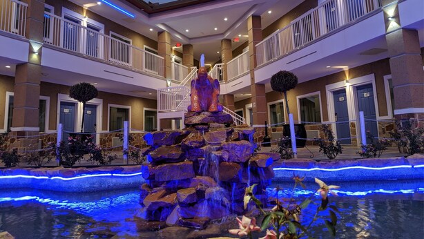 A hotel lobby with a central rock fountain, multiple balconies, and a staircase leading to the upper floor. - Motel 6 Houston, TX - North (Houston)