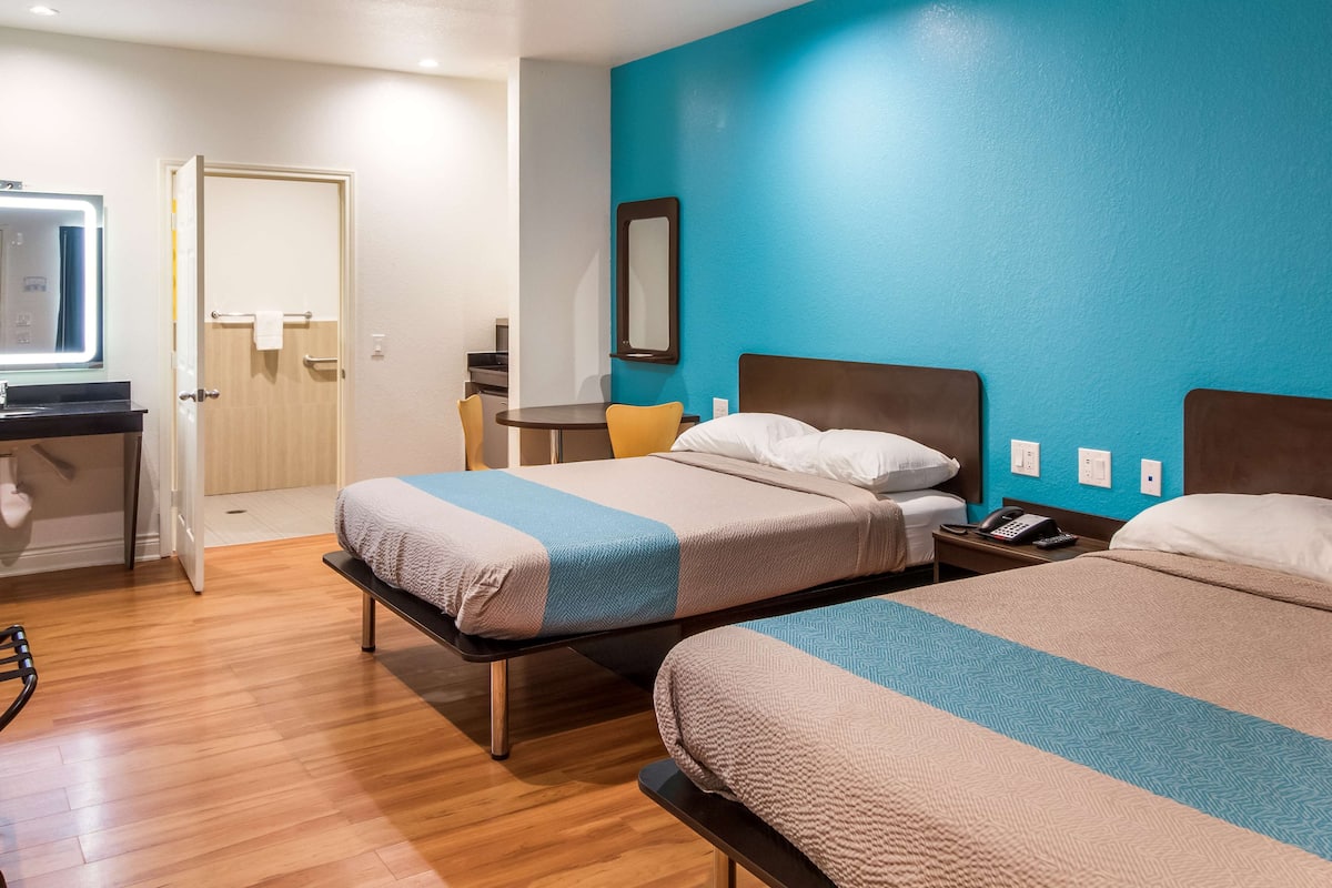 A hotel room with two beds, a desk, a chair, and a bathroom.