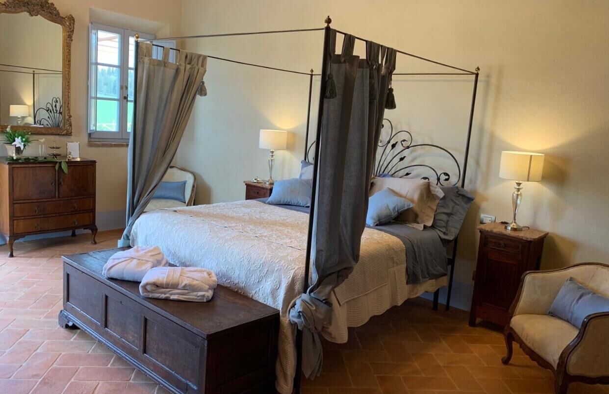 Un lit à baldaquin à quatre poteaux avec une tête de lit en bois, deux tables de chevet avec des lampes, une commode en bois et une chaise.