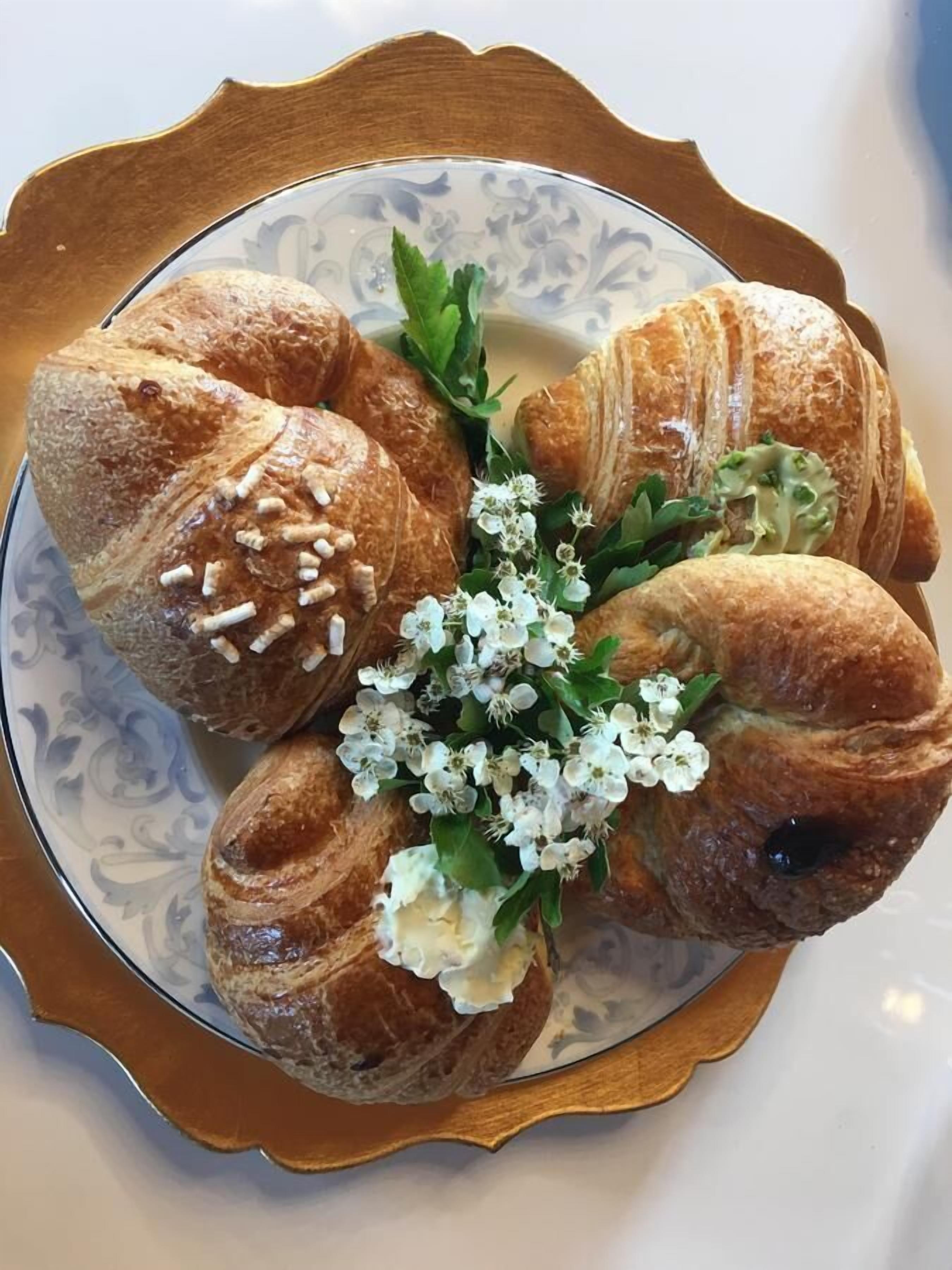 A plate of croissants with a decorative arrangement of flowers and greenery.