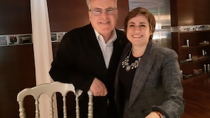 A man and a woman standing in a room with wooden furniture and a white chair.