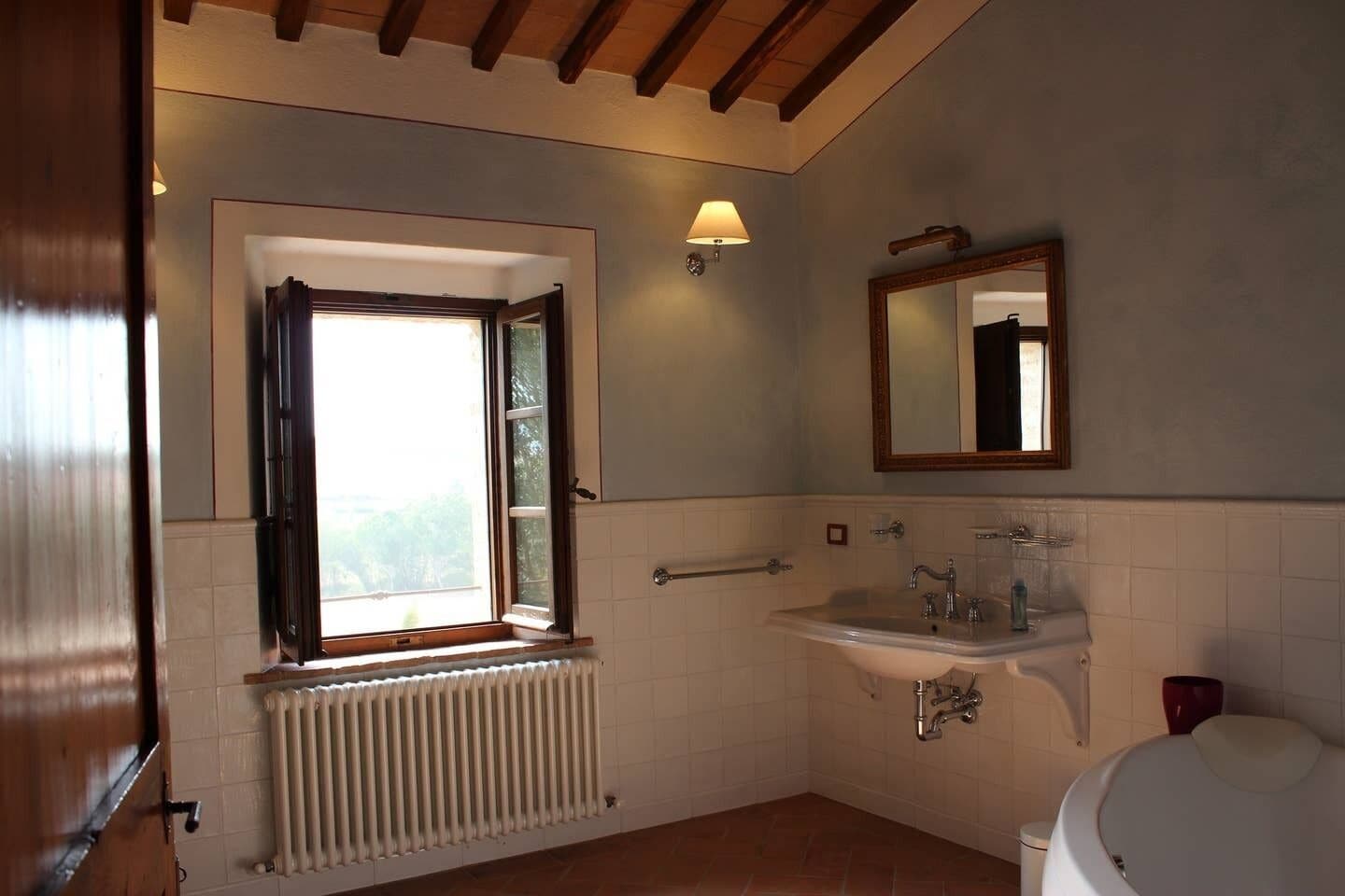 Une salle de bain avec une fenêtre, un lavabo, un miroir et des toilettes.