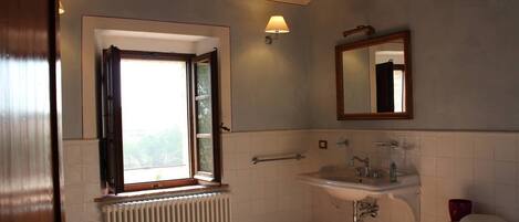 A bathroom with a window, a sink, a mirror, and a toilet.