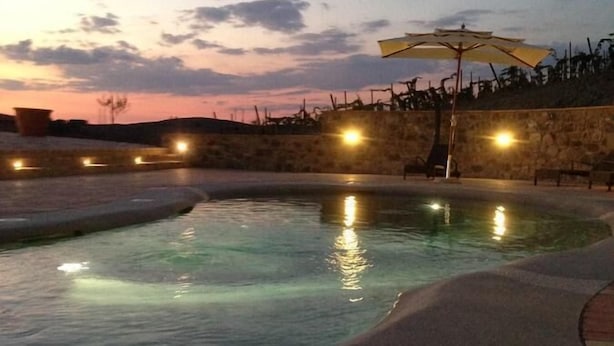 A swimming pool with a stone wall and a bench, surrounded by lights.