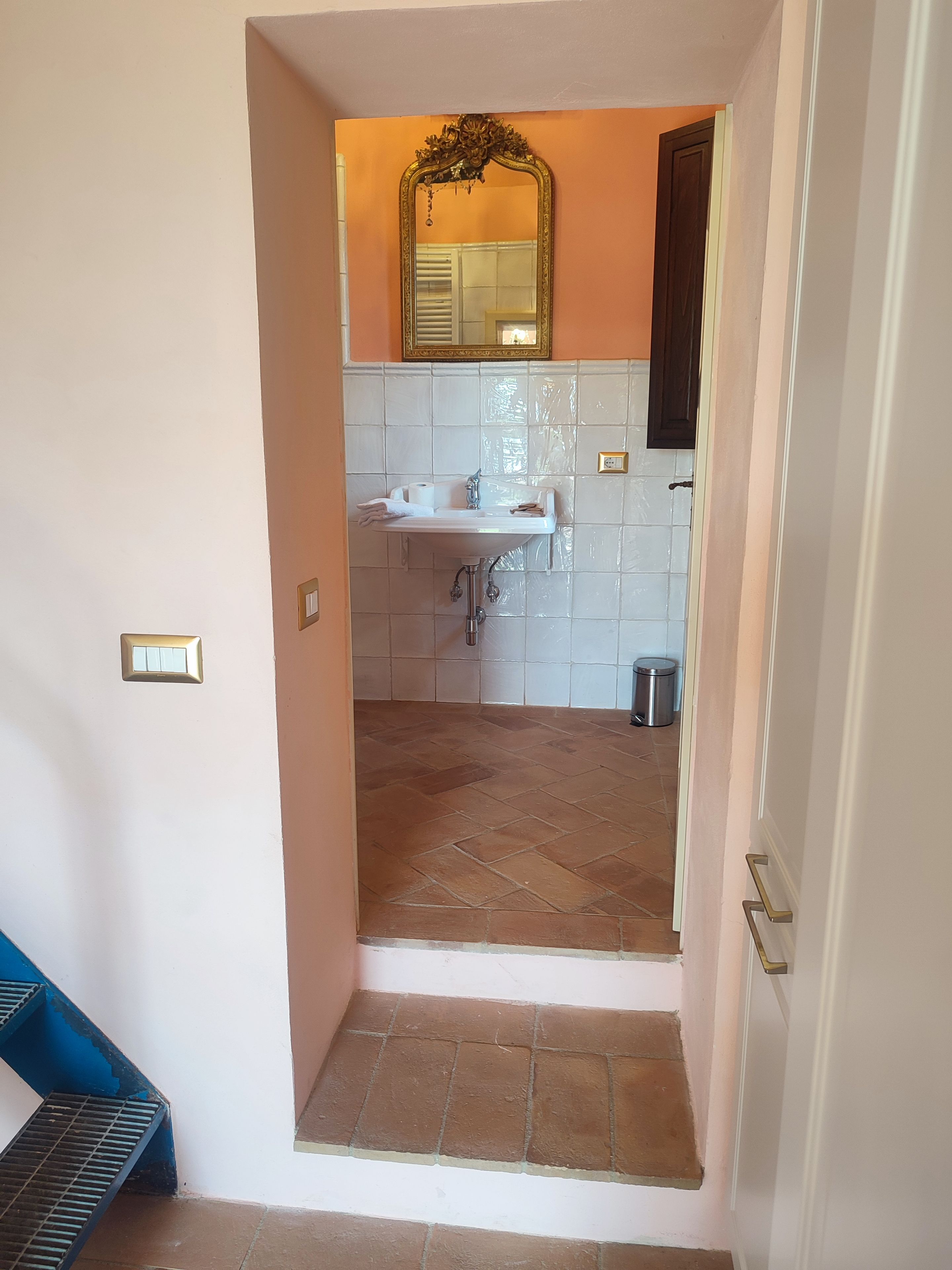 A narrow hallway leading to a bathroom with a sink, mirror, and tiled walls.