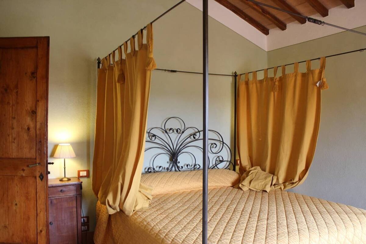 A four-poster bed with yellow curtains, a wooden wardrobe, and a metal headboard.