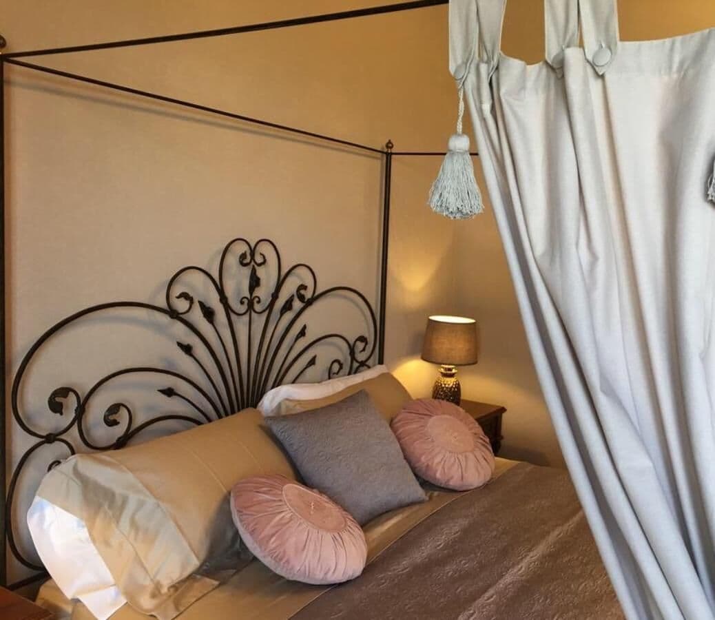 Un lit avec une tête de lit en métal, plusieurs oreillers, une lampe de chevet et un baldaquin.