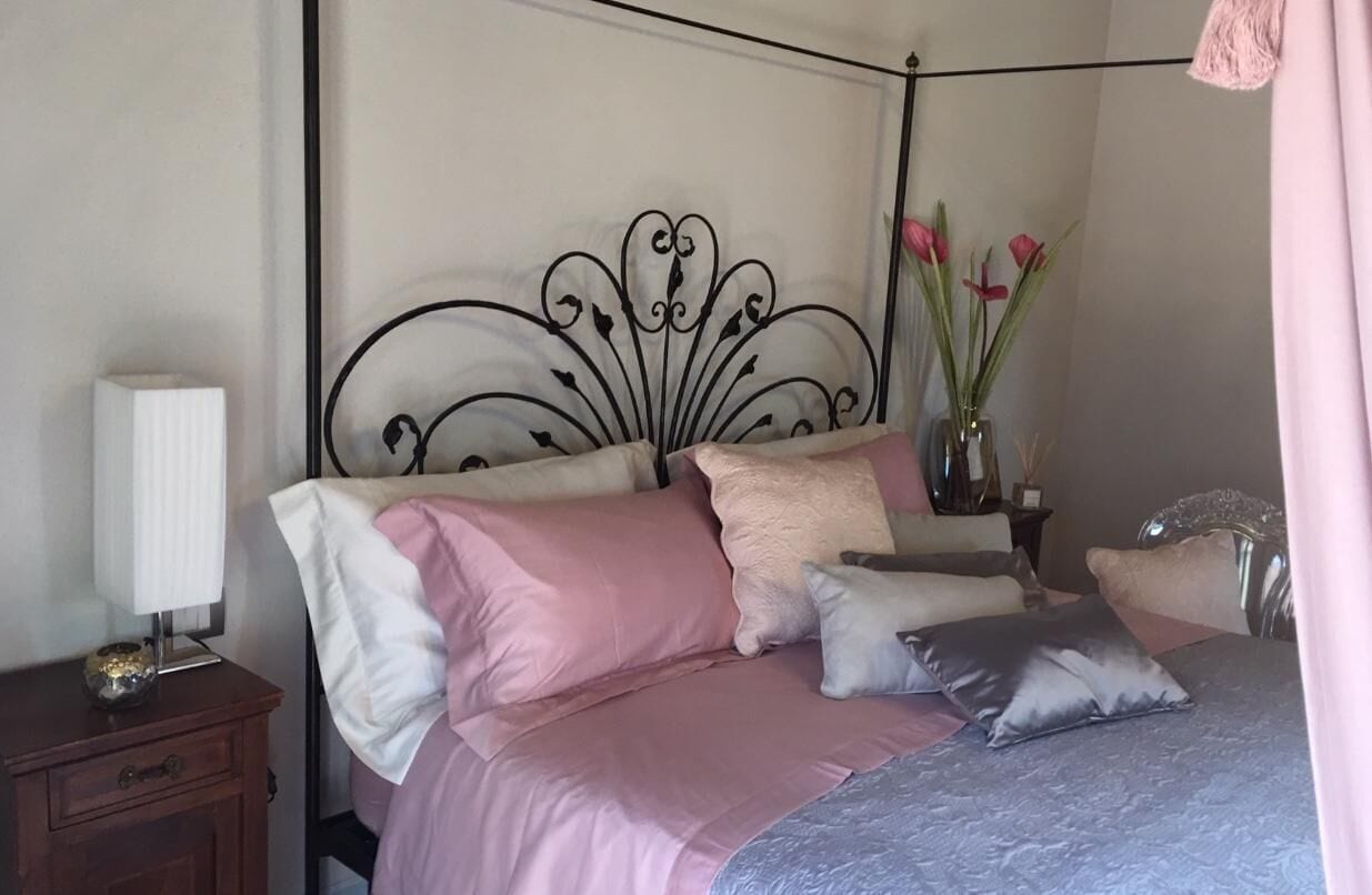 Une chambre à coucher avec une tête de lit en métal, une table de chevet avec une lampe et un vase rempli de fleurs.