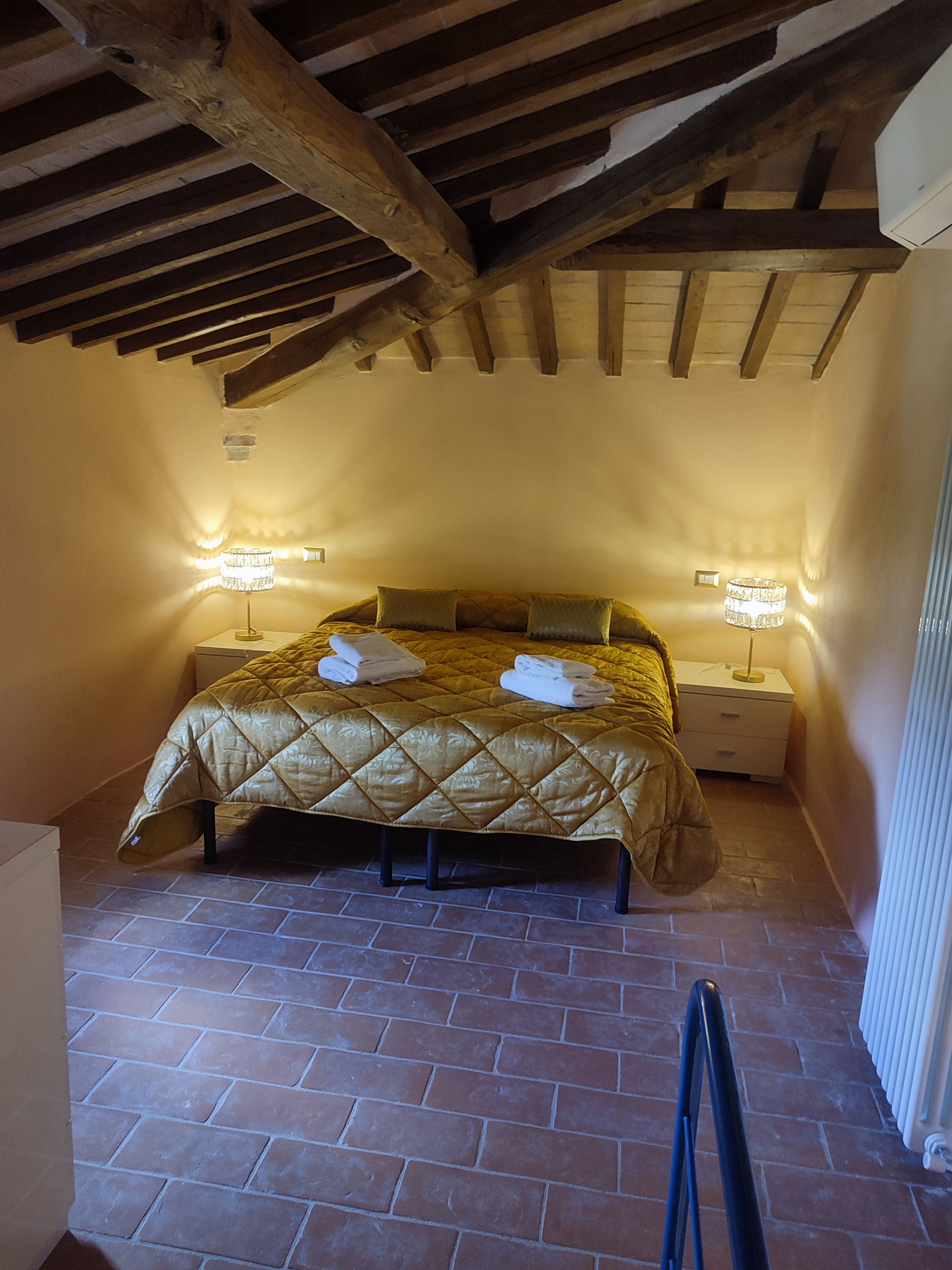 A bedroom with a bed, two bedside lamps, a radiator, and a tiled floor.
