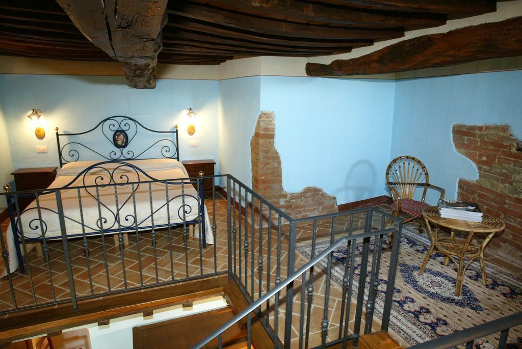 A bedroom with a bed, a chair, a small table, and a staircase.