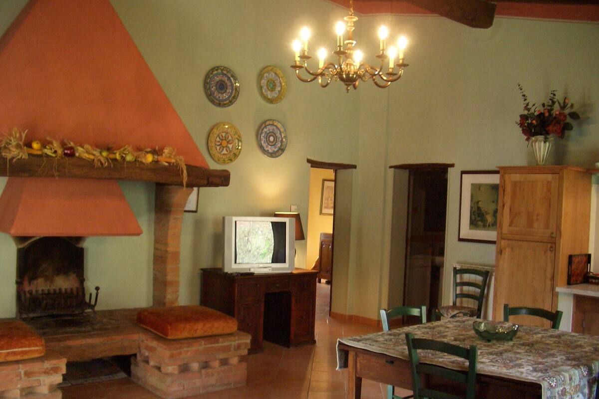 Un área de comedor con chimenea de ladrillo, un televisor sobre un soporte de madera y una araña.