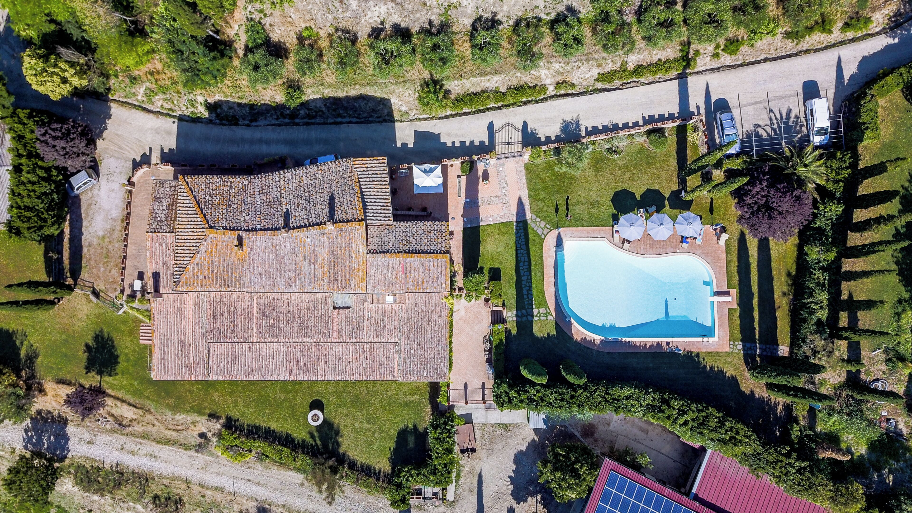 Vista aérea de una propiedad con piscina, un edificio grande con techo de tejas y un camino de entrada pavimentado.