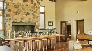 A spacious room with a stone fireplace, wooden ceiling beams, and a long bar area with stools. - Casa de Huespedes Gimenez Riili (Tunuyan)