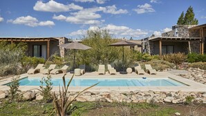 A pool area with lounge chairs and umbrellas, surrounded by a natural landscape and stone buildings. - Casa de Huespedes Gimenez Riili (Tunuyan)