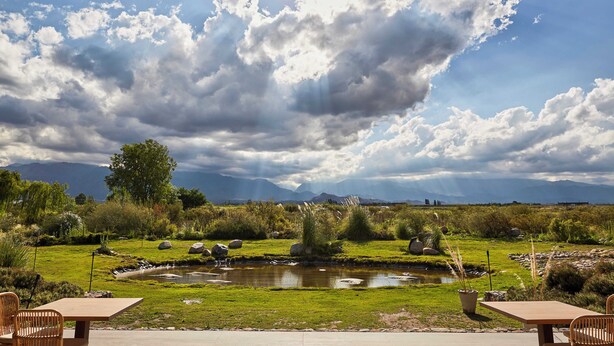 A serene outdoor setting with a wooden pergola, a small pond, and a grassy area with rocks and plants. - Casa de Huespedes Gimenez Riili (Tunuyan)