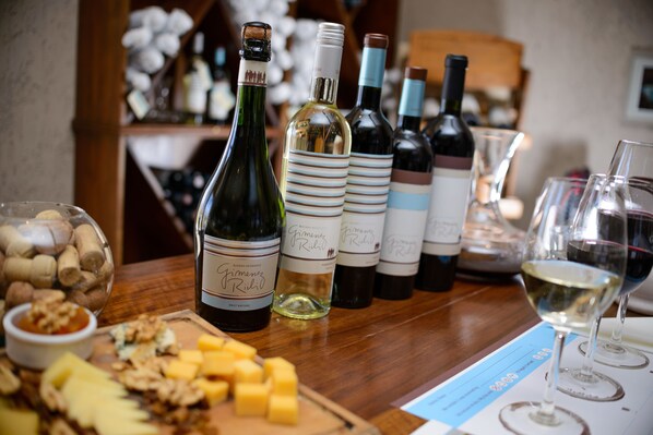 A wine tasting setup with various bottles and glasses on a wooden table, accompanied by cheese and nuts.