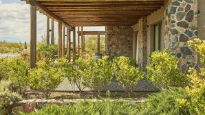 A covered outdoor area with stone walls and wooden beams, surrounded by various shrubs and plants. - Casa de Huespedes Gimenez Riili (Tunuyan)
