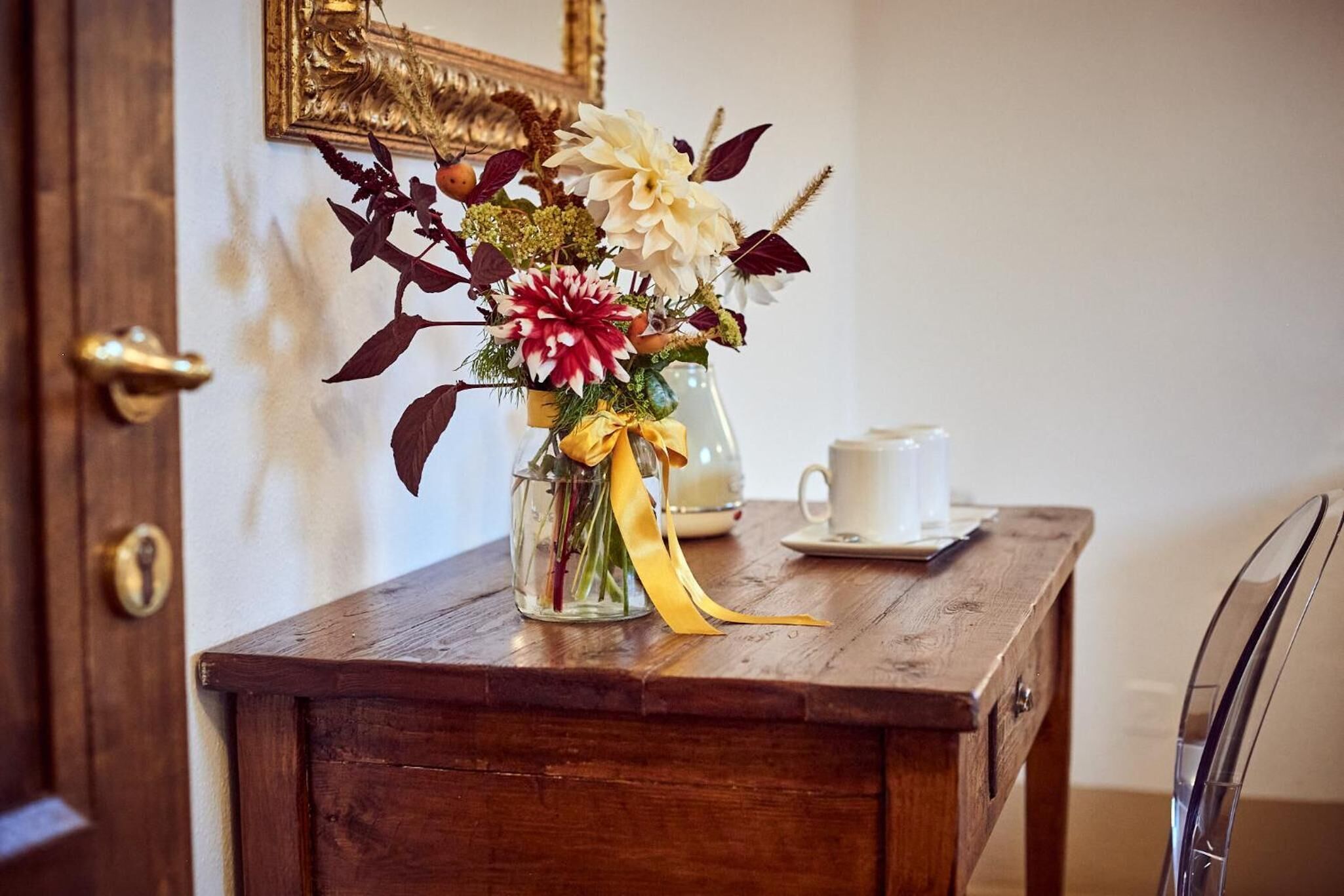 Une table en bois sur laquelle se trouve un vase en verre contenant un bouquet de fleurs et un ruban jaune.