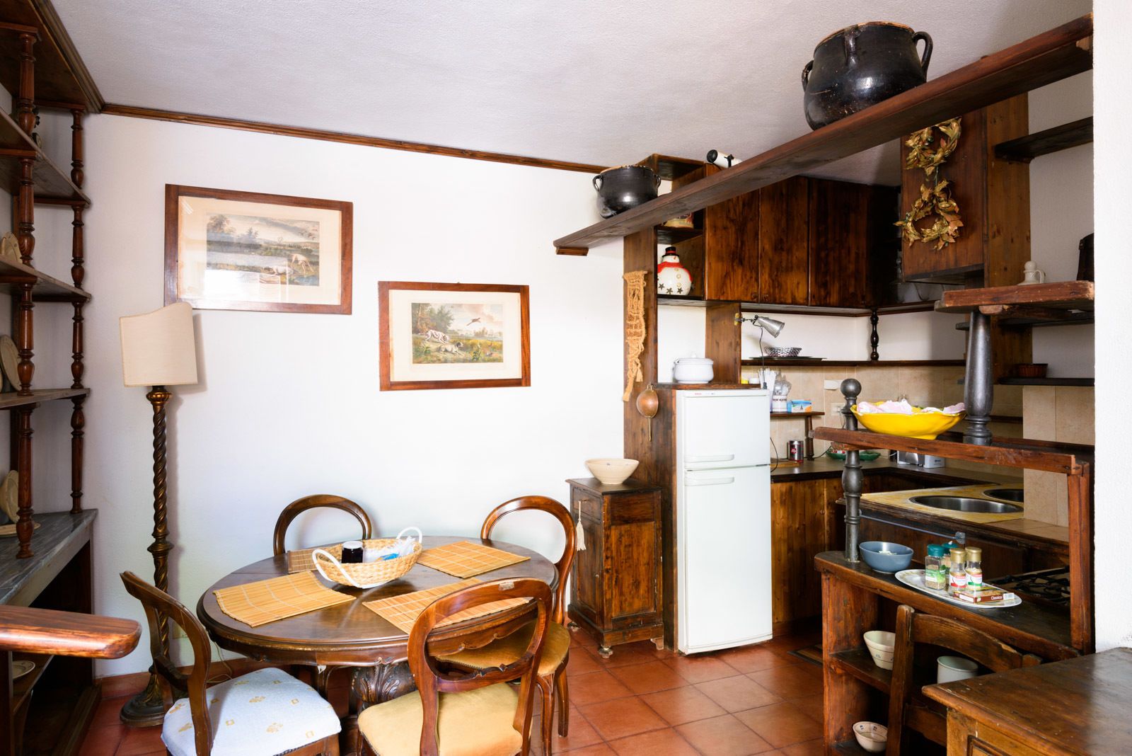 Une cuisine de taille réduite, dotée de meubles en bois, d’une table à manger avec des chaises, d’un réfrigérateur et d’un évier.