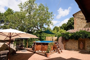 Un patio con un jacuzzi de madera, mobiliario exterior y un muro de piedra.