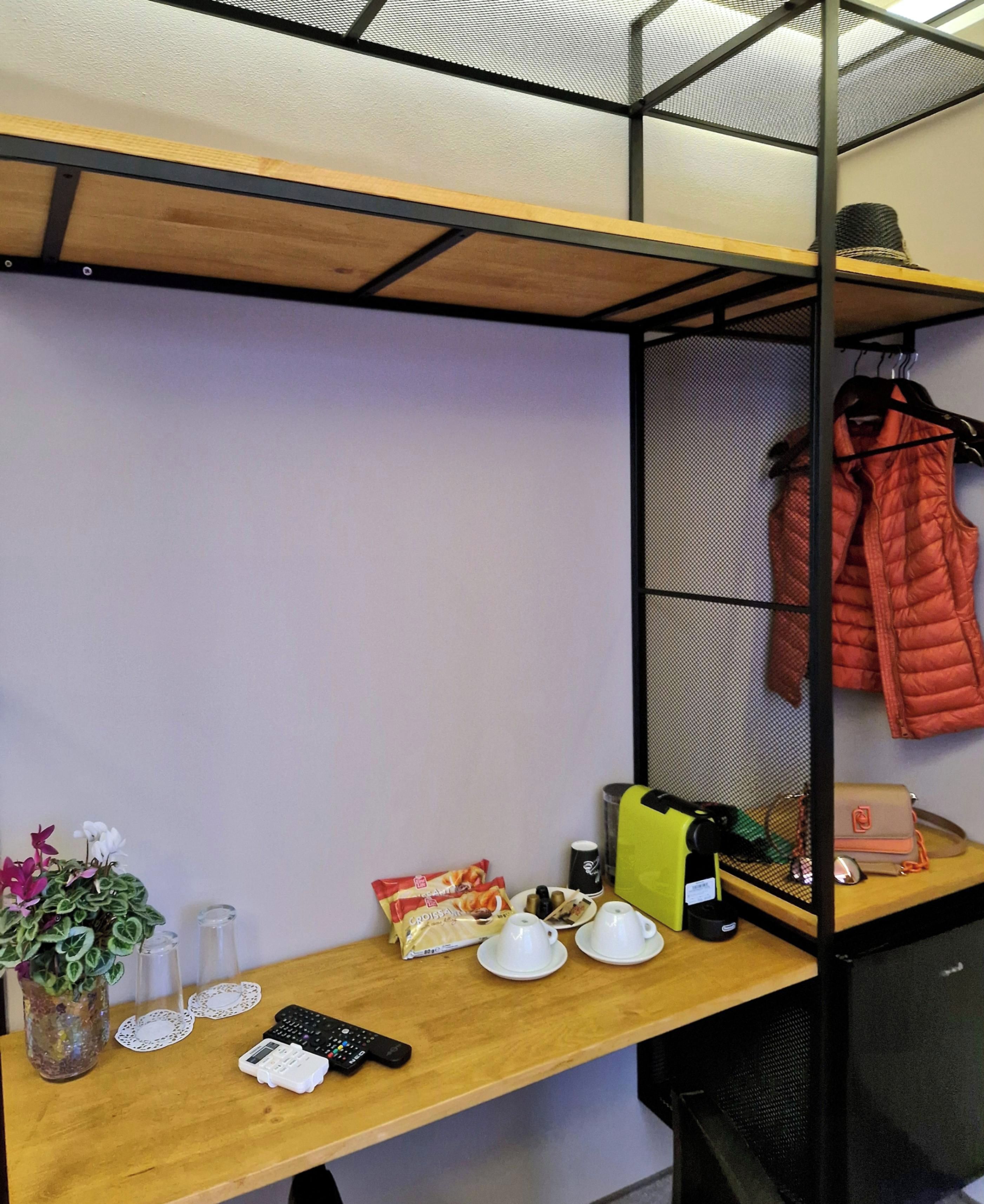 Une pièce avec un bureau en bois, une étagère sur laquelle est posée une veste, une machine à café et une plante.