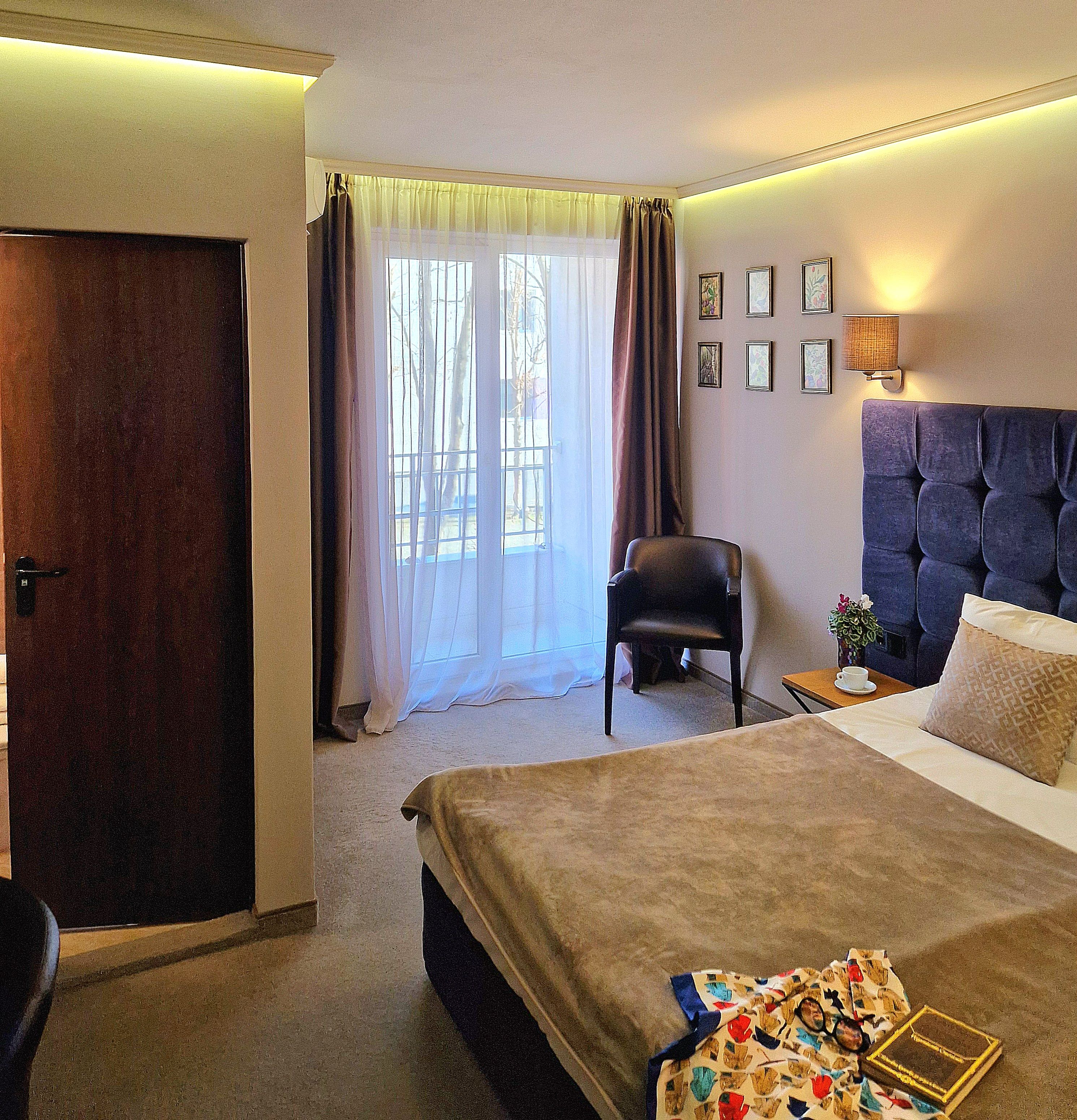 Una habitación de hotel con cama, una silla, un escritorio con lámpara y una ventana con cortinas.