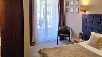Una habitación de hotel con cama, una silla, un escritorio con lámpara y una ventana con cortinas.